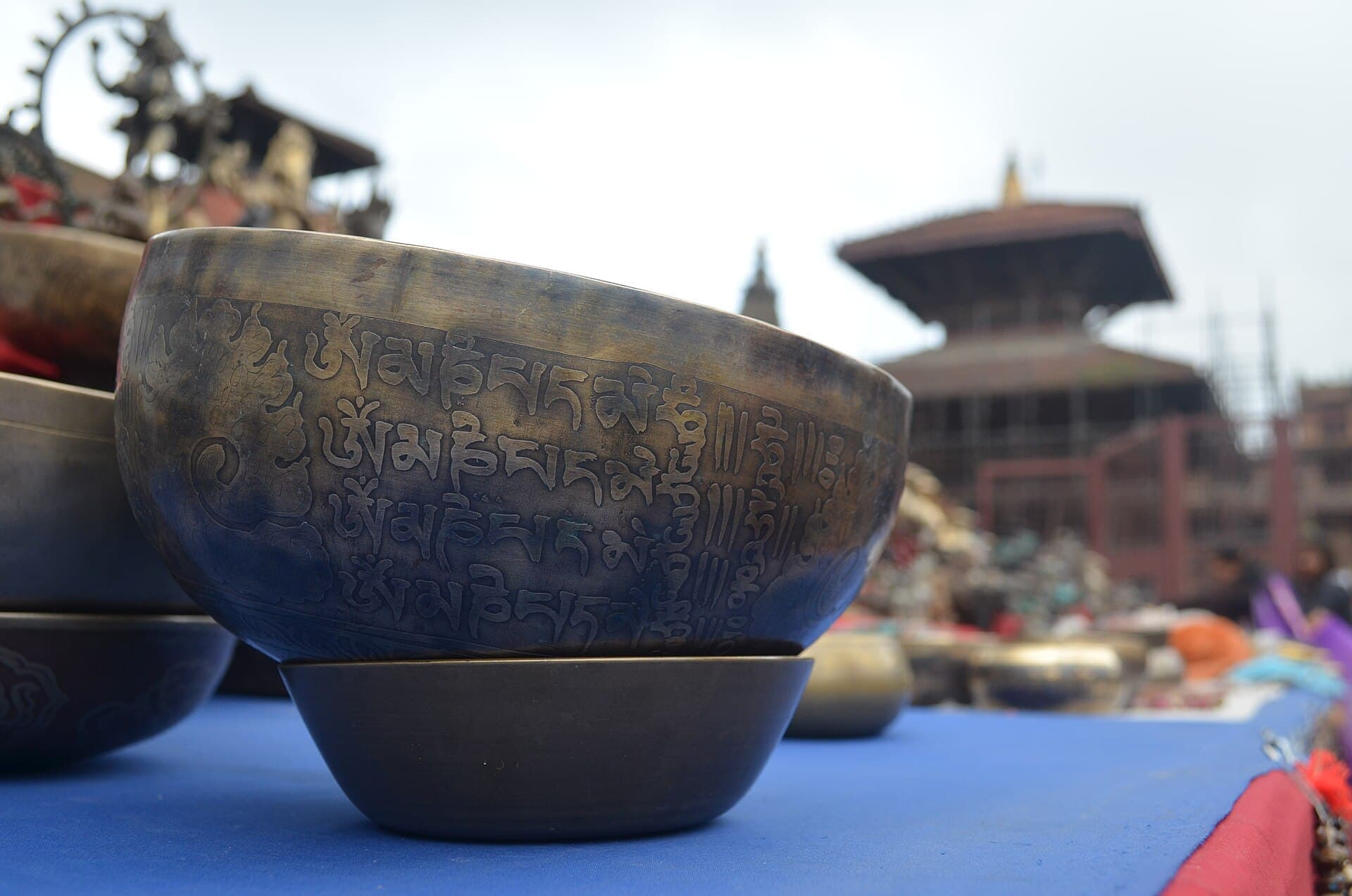 Hand-hammered singing bowls displayed in a square with a pagoda temple behind, Nepal