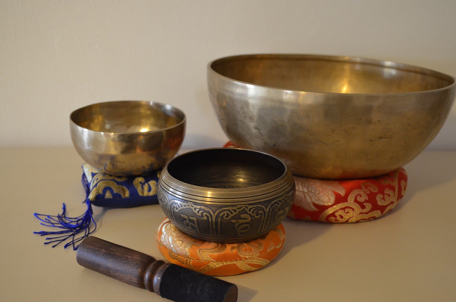 Three bronze singing bowls of different sizes with cushions and a wooden mallet